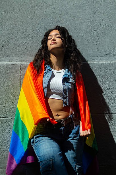 istock Young latin woman leaning against wall with rainbow flag 2207743467