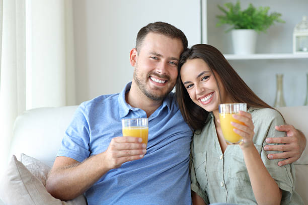 istock Happy couple drinking orange juice looking at camera 2207743787