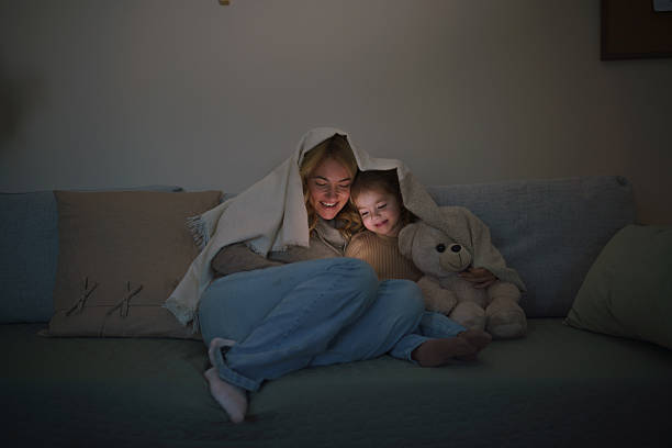istock Mother and daughter sitting on sofa during the night and using mobile phone 2207743843