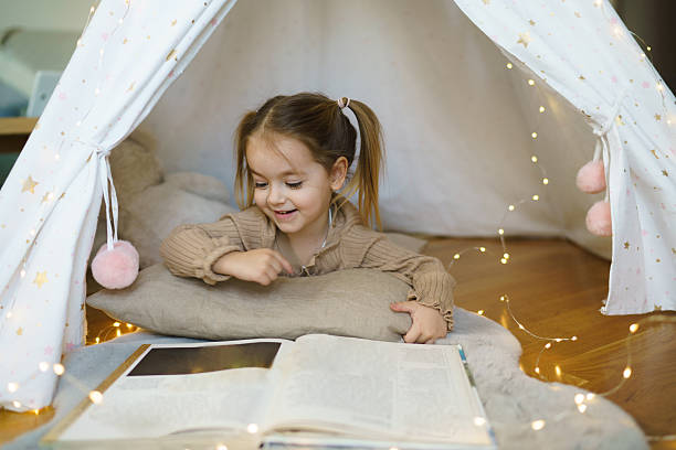 istock Girl looking at book while lying in tent 2207744838