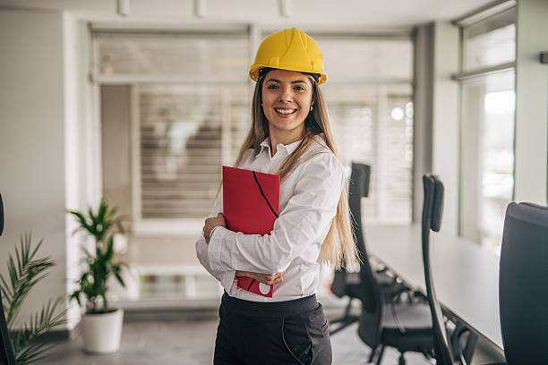 Smiling female architect holding plans wearing hard hat in office