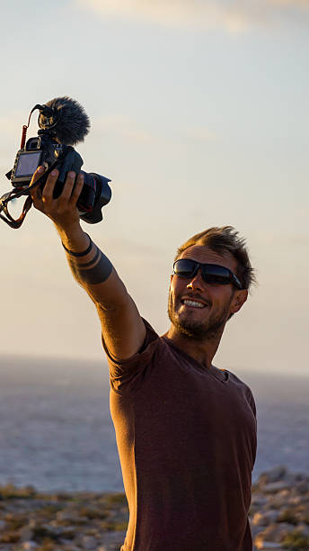 istock Photographer capturing sunset moments on the coast with a camera in hand 2207749670
