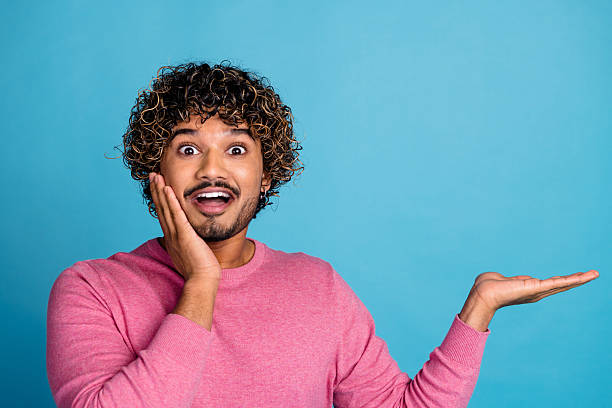 istock Young stylish male with expressive gestures in casual pink pullover on bright blue background showcasing cheerful emotion and enthusiasm 2207750844