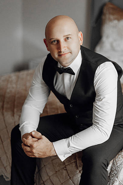 istock A man wearing a black vest and a black bow tie sits on a bed 2207752058