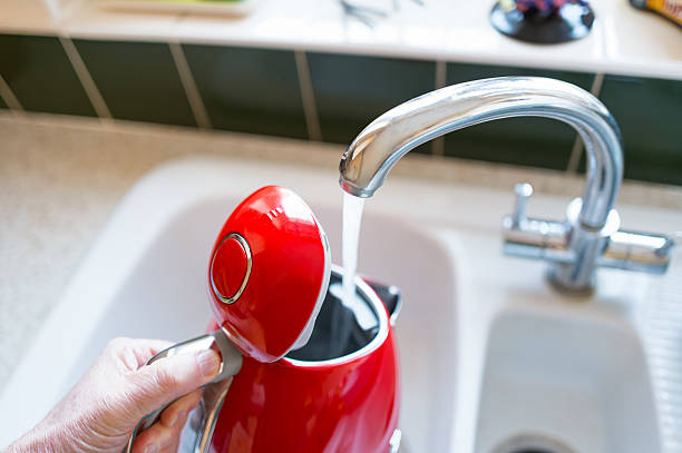 Homeowner seen filling a stylish water kettle at a kitchen sink. stock photo