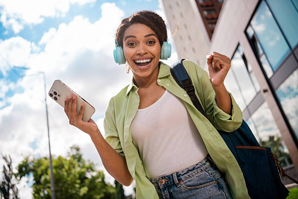 istock Cheerful young woman enjoying music while using smartphone outdoors in urban setting 2207758168