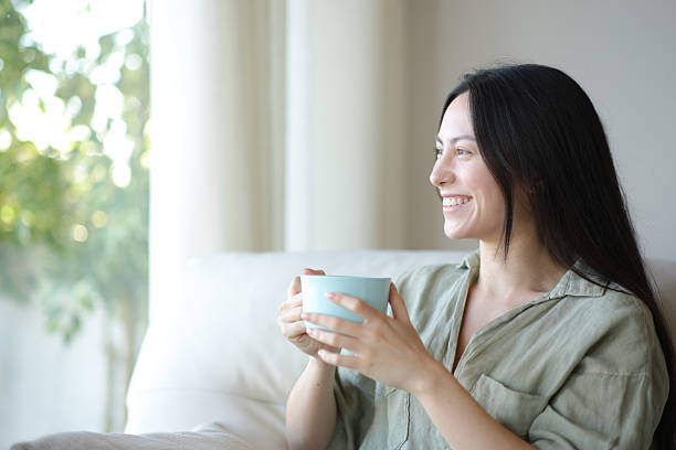 istock Happy asian woman drinking and looking through a window 2207761960