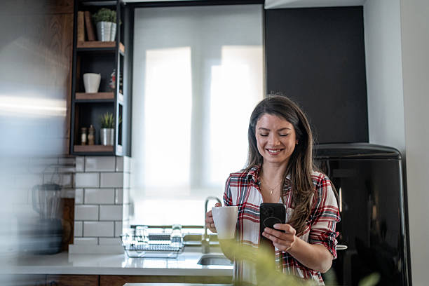 istock Smiling woman enjoying morning coffee and using smartphone in modern kitchen 2207762541