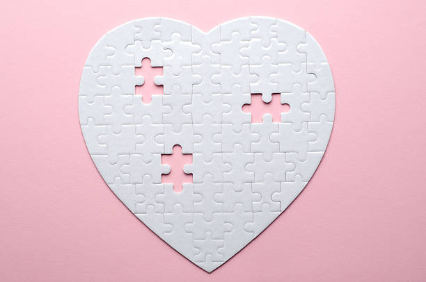 White heart-shaped jigsaw puzzle on a grey background, with several pieces missing and placed nearby. Symbolizing love, connection, or incompleteness, perfect for themes of relationships and emotions.