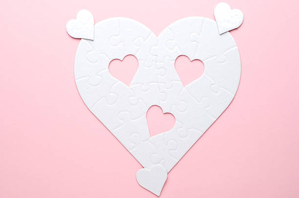 White heart-shaped jigsaw puzzle on a grey background, with several pieces missing and placed nearby. Symbolizing love, connection, or incompleteness, perfect for themes of relationships and emotions.