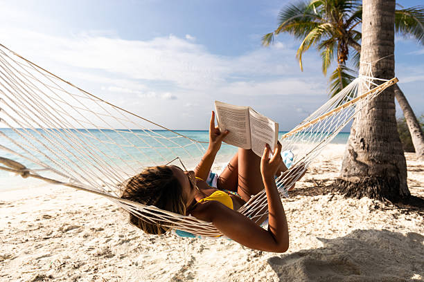 Relaxed woman reading a book in hammock on the beach.