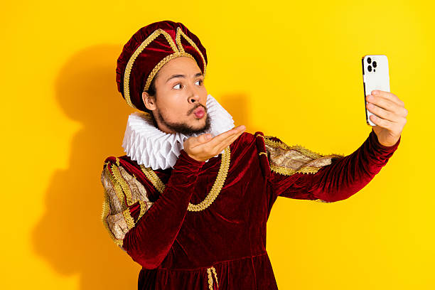 istock Young man dressed as a historical nobleman takes a selfie with a modern smartphone against a vibrant yellow background, blending past and present styles. 2207766607
