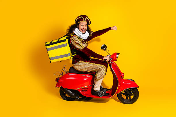 istock Young man in a historical costume riding a red scooter with a large backpack against a vibrant yellow background 2207766627