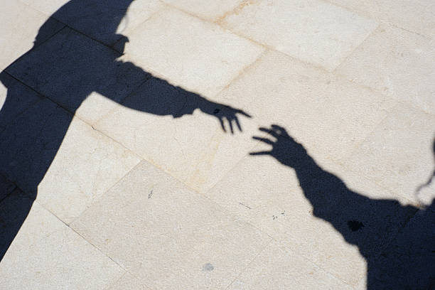 istock Shadows of two hands reaching out on sunlit pavement 2207777475