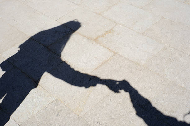 Shadows of people holding hands on sunlit pavement.