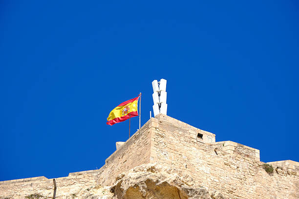 istock Spanish flag fluttering on santa barbara castle against a clear blue sky 2207777855