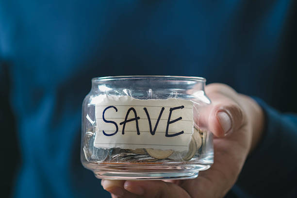 Hand holding jar filled with coins labeled 'SAVE', representing financial savings, budgeting, and personal finance. Ideal for banking or investment themes.