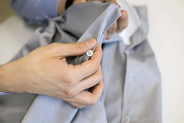 Production process of custom made male shirt. tailor concentrated on sewing buttons, close-up shot