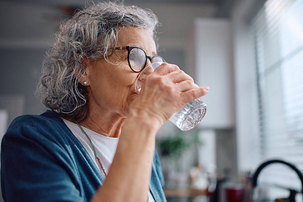 Senior woman drinking water in kitchen.