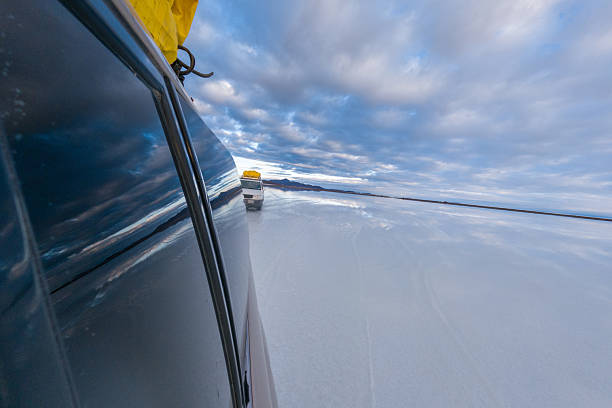 Van traversing Bolivia's vast salt flats. Vehicle mirrored on expansive reflective surface. Adventure and exploration in Salar de Uyuni's unique landscapes.