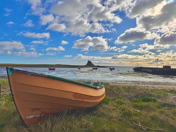 Three moored fishing boats in the channel off Holy Island, UK. In the background is one of the two Old Law Beacons, now a lighthouse, that when lined up guide ships into the harbour.