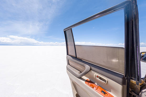 Vehicle door ajar against vast salt flat under blue sky. Open car door revealing vast horizon. Travel adventure in isolated, pristine landscape.
