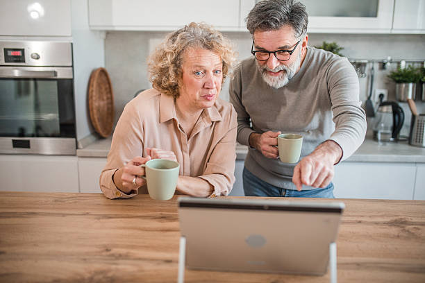 istock Cheerful mature couple using laptop while standing at kitchen counter drinking coffee 2207794534