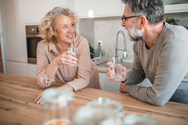 istock Smiling mature couple refreshing themselves by drinking water while standing at the kitchen counter 2207795901