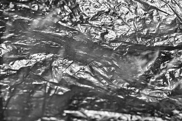 Crumpled aluminum foil texture, close-up view. The intricate details and reflective surface highlight the creases and folds, suitable for backgrounds, textures, and abstract themes.