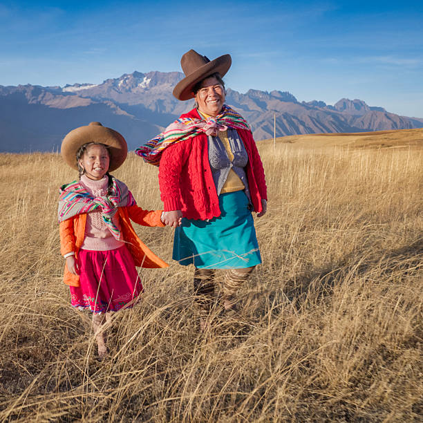 Peruvian young mother in traditional clothing crossing a field with her baby boy, Peruvian Andes on the background, The Sacred Valley.The Sacred Valley of the Incas or Urubamba Valley is a valley in the Andes  of Peru, close to the Inca capital of Cusco and below the ancient sacred city of Machu Picchu. The valley is generally understood to include everything between Pisac  and Ollantaytambo, parallel to the Urubamba River, or Vilcanota River or Wilcamayu, as this Sacred river is called when passing through the valley. It is fed by numerous rivers which descend through adjoining valleys and gorges, and contains numerous archaeological remains and villages. The valley was appreciated by the Incas due to its special geographical and climatic qualities. It was one of the empire's main points for the extraction of natural wealth, and the best place for maize production in Peru.