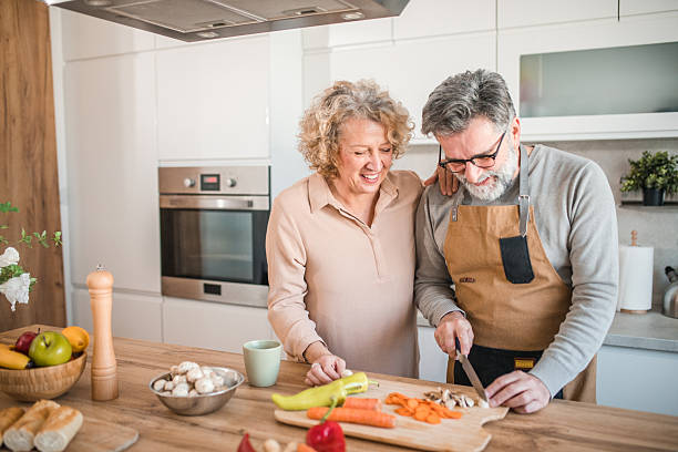 istock A cheerful man in an apron is chopping vegetables on a cutting board at the kitchen counter, in the company of his smiling wife 2207798049