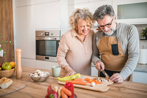 istock A cheerful man in an apron is chopping vegetables on a cutting board at the kitchen counter, in the company of his smiling wife drinking coffee 2207798616