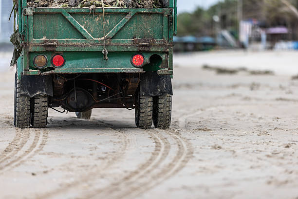 Green vehicle is moving on sands at beach.