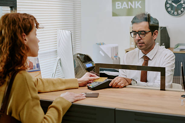 istock Customer Engaging with Bank Teller through Counter Glass 2207802649