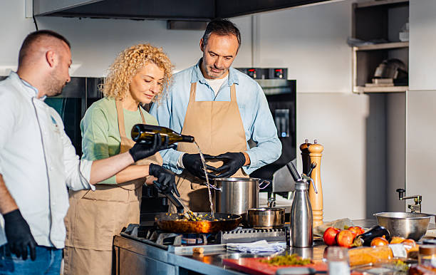 Couple enjoying a cooking class with a chef preparing meal in the kitchen.