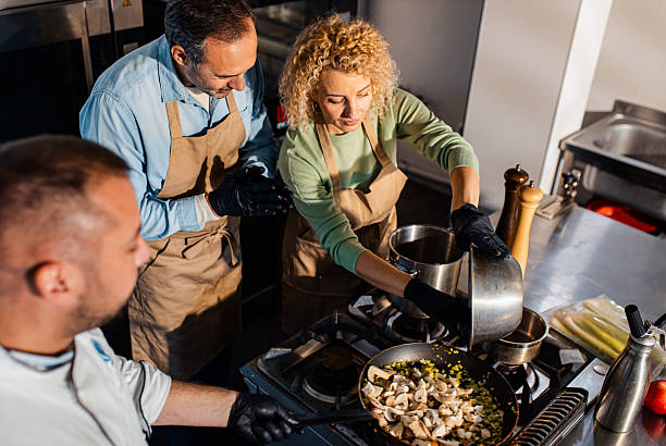 Couple enjoying a cooking class with a chef preparing meal in the kitchen.