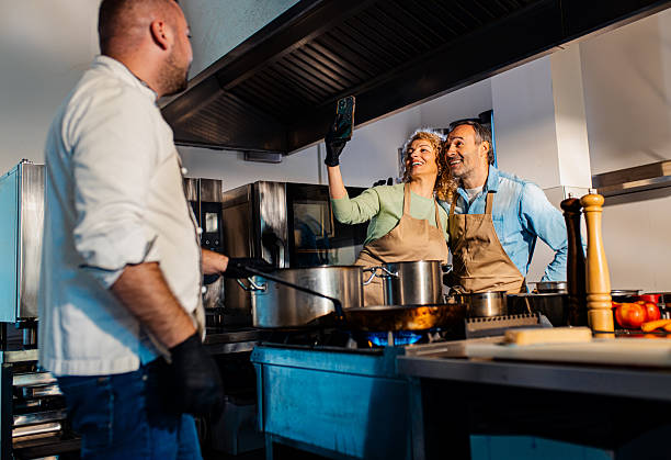 Couple making selfie at cooking class with a chef preparing in the kitchen.