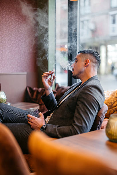 istock Young Man Smoking A Cigar While Drinking Whiskey In A Bar 2207806943