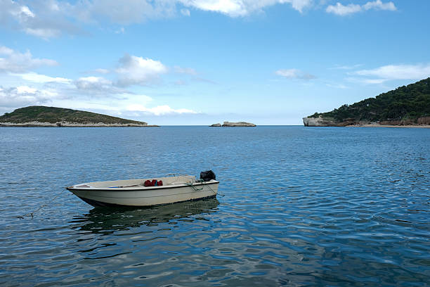 Lonely boat floating on calm blue sea with islands in background, wide angle view.