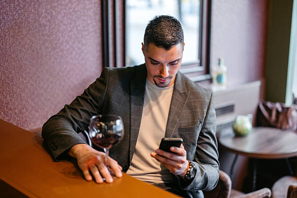 istock Young Man Using Phone While Drinking A Glass Of Red Wine In A Bar 2207807663