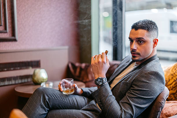 istock Young Man Smoking A Cigar While Drinking Whiskey In A Bar 2207807686