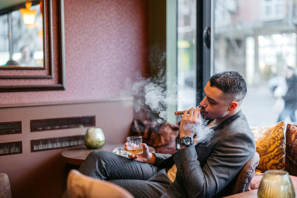istock Young Man Smoking A Cigar While Drinking Whiskey In A Bar 2207807827