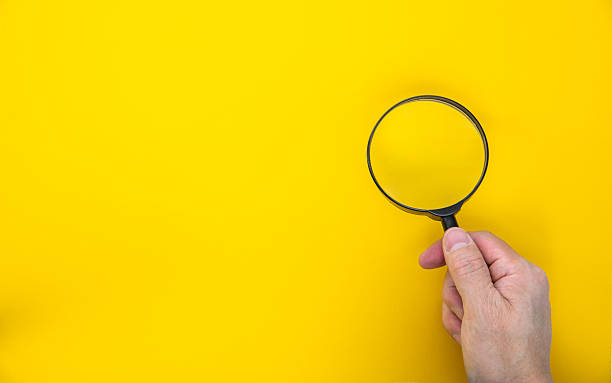 istock Man hand holding a magnifying glass on orange background 2207807917