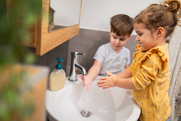 istock Siblings washing their hands with liquid soap and water in modern home bathroom, learning independence and good hygiene 2207810395