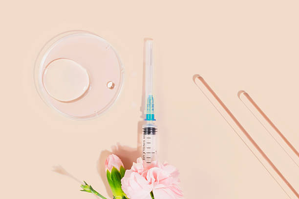 Syringe with pink flowers, lab tools, and petri dish on nude background
