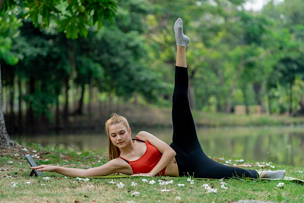 A young woman practices exercise and yoga in serene park setting, stretching gracefully while enjoying peaceful surroundings. Her focus and determination shine through as she connects with nature