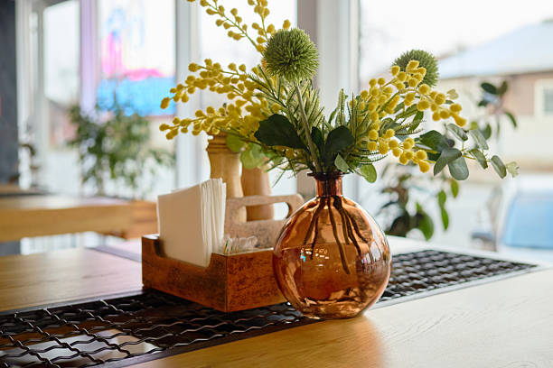 A warm and inviting cafe showcases a beautifully arranged table with a decorative vase filled with flowers, complementing the contemporary atmosphere. Natural light streams through large windows