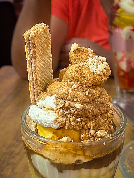 Delicious ice cream sundae with whipped cream wafers caramel and nuts served in a glass dessert cup.