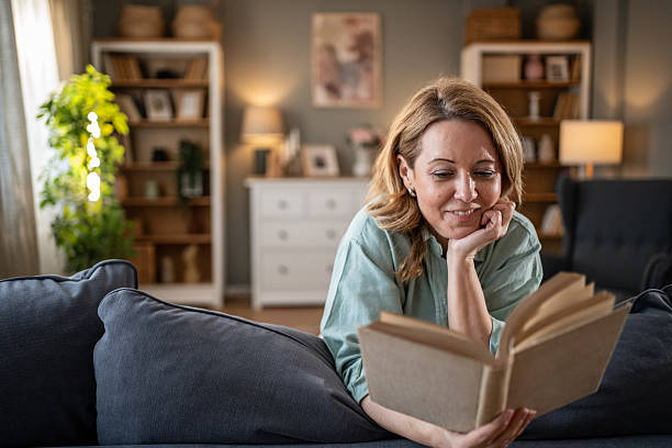 istock Smiling woman reading a book on the sofa at home 2207839415