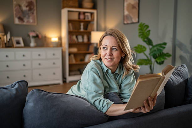 istock Smiling woman relaxing on sofa reading a book at home 2207839485